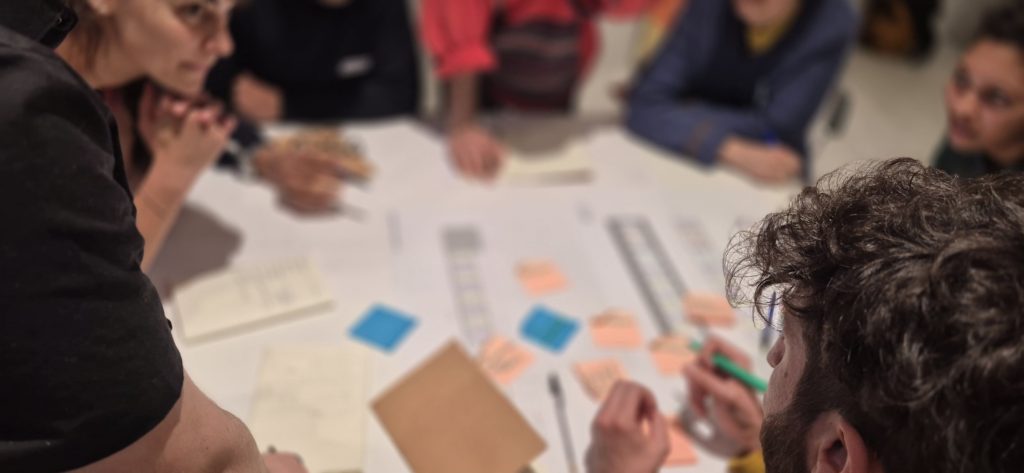 Alcuni partecipanti fotografati dall'alto mentre incollano post-it su una piantina dello stabile Fioravanti 24 e prendono appunti durante un laboratorio
