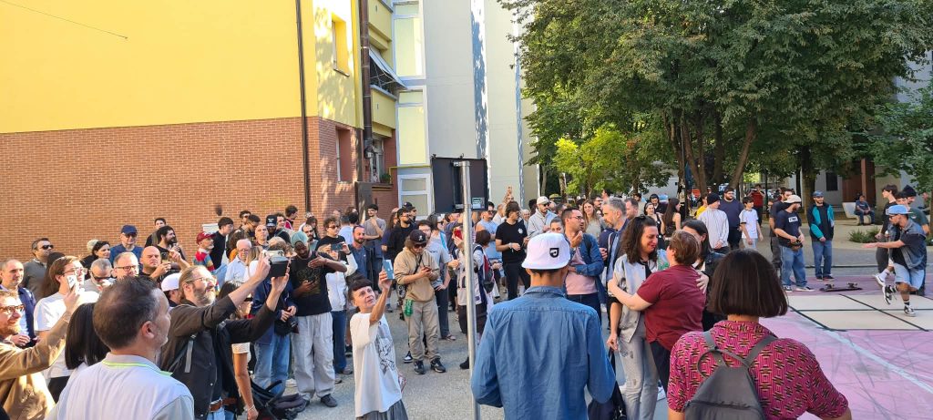 una folla di persone presenti all'intitolazione del giardino con sullo sfondo i palazzi delle popolarissime