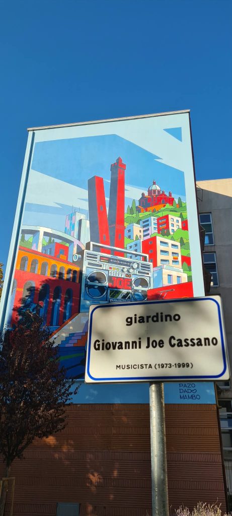 Il nuovo murale dei 120 anni di ACER sullo sfondo della targa che intitola il giardino a Giovanni Joe Cassano musicista (1973 - 1999(